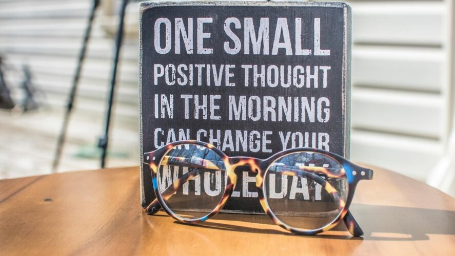 Eyeglasses resting on a table in front of a motivational quote sign, emphasizing positivity.