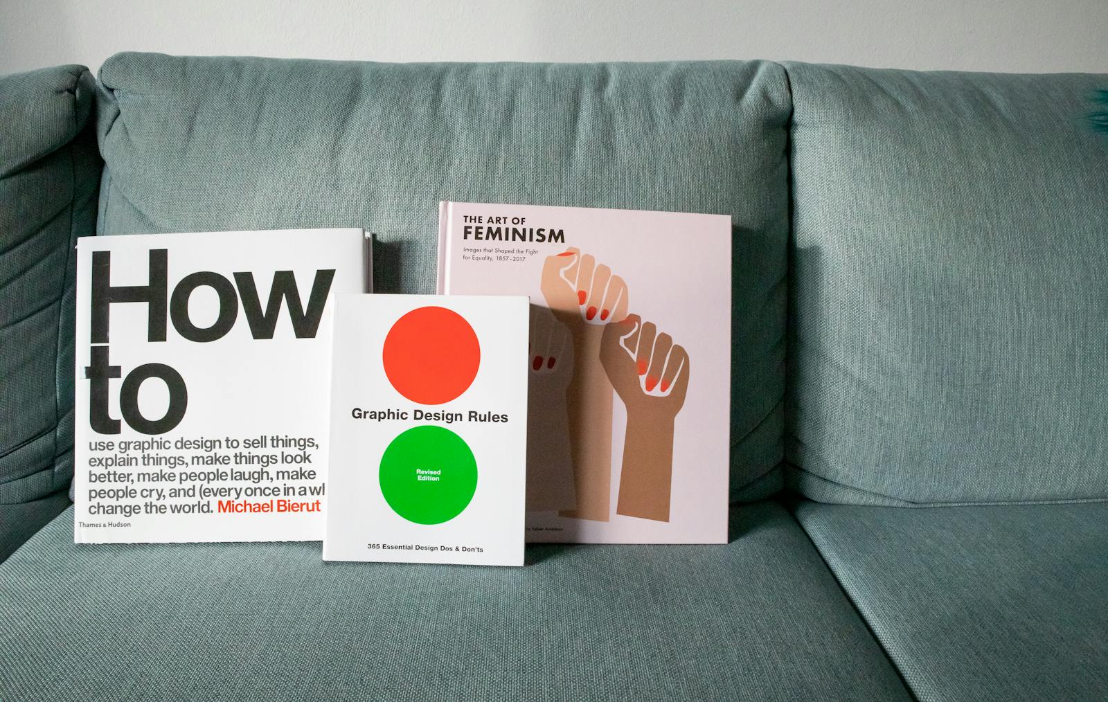Three design and feminism books displayed on a sofa, highlighting graphic design themes.