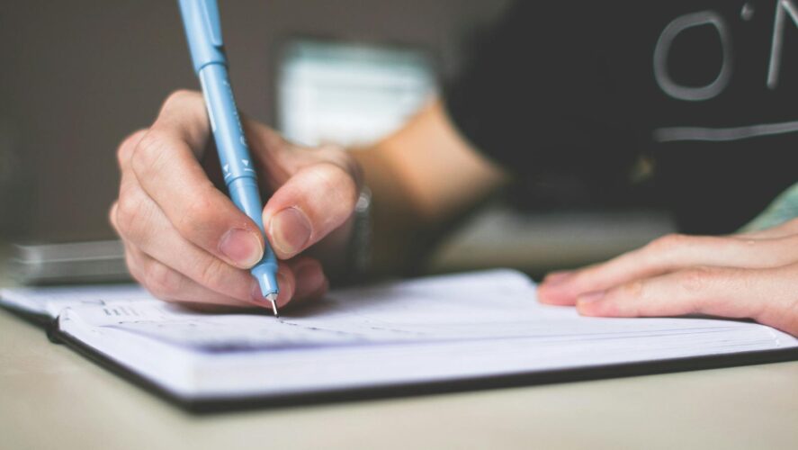 Close-up of hand writing in notebook using a blue pen, focus on creativity.