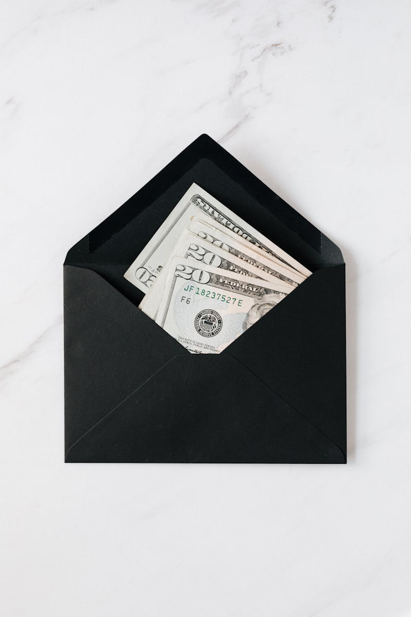 Top view of opened envelope with USA banknotes of 20 dollars placed on white marble desk illustrating concept of money gift or charity