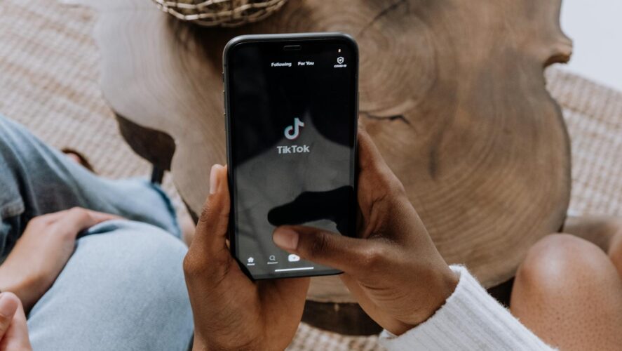 Close-up of hands holding a smartphone displaying the TikTok app interface on a wooden surface.